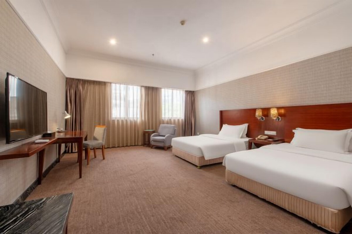 A hotel room with two beds, a TV, a desk, and a chair.