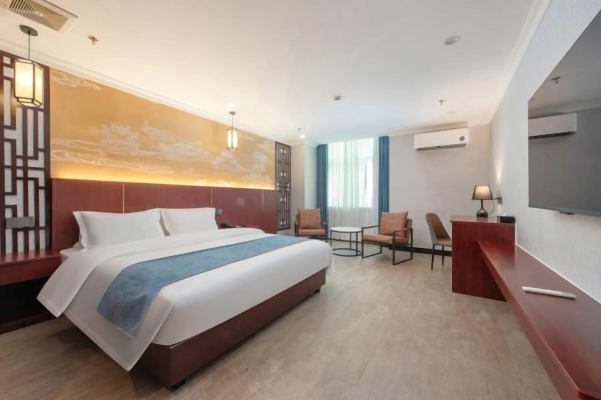 A hotel room with a large bed, a desk, a chair, a TV, and a window with curtains.