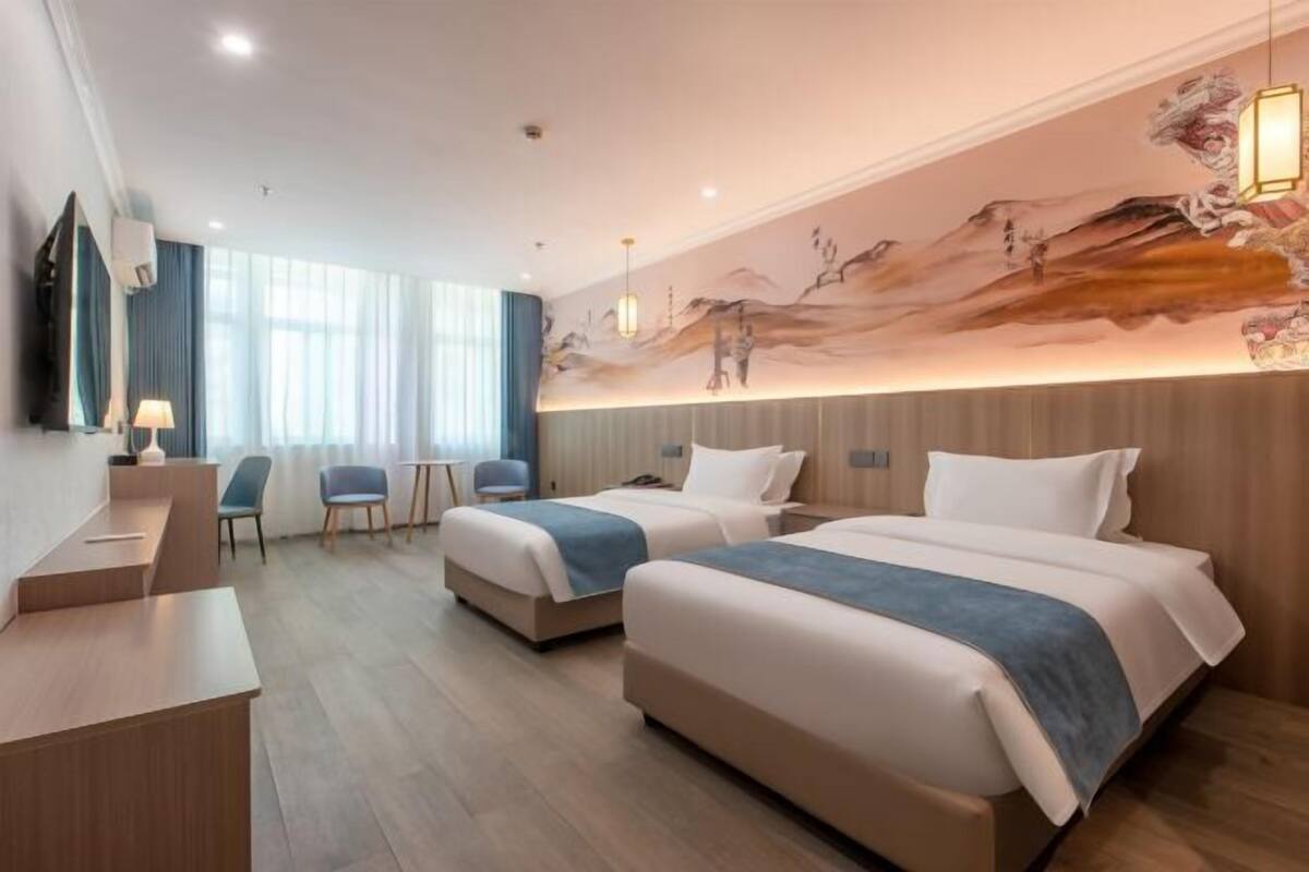A hotel room with two beds, a desk, chairs, and a large mural on the wall.