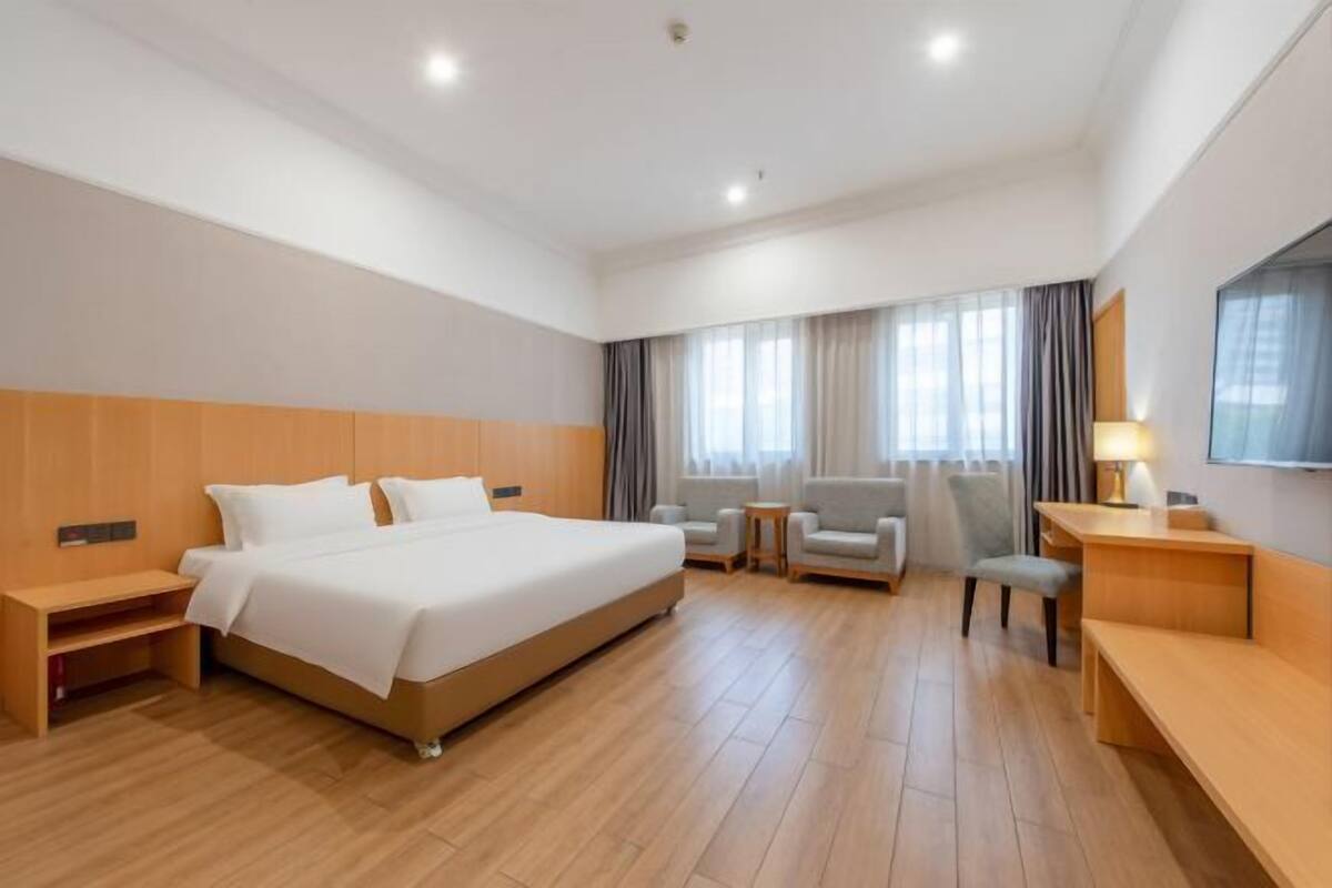 A hotel room with a large bed, a desk, a chair, a sofa, and a TV.