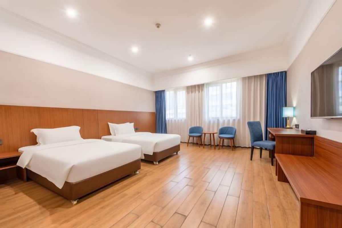 A hotel room with two beds, a desk, a chair, a TV, and a window with curtains.