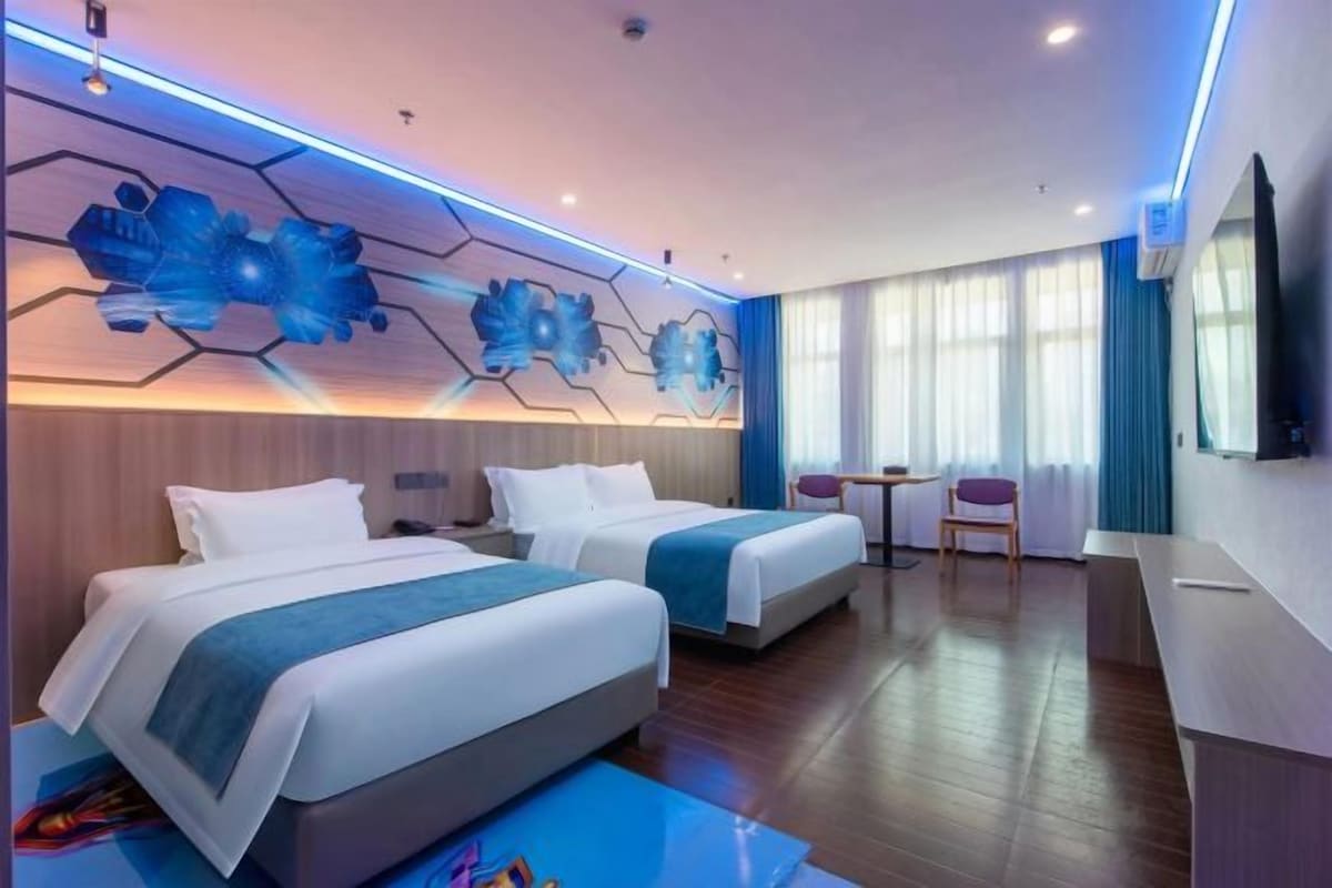 A hotel room with two beds, a desk, a chair, and a large window.