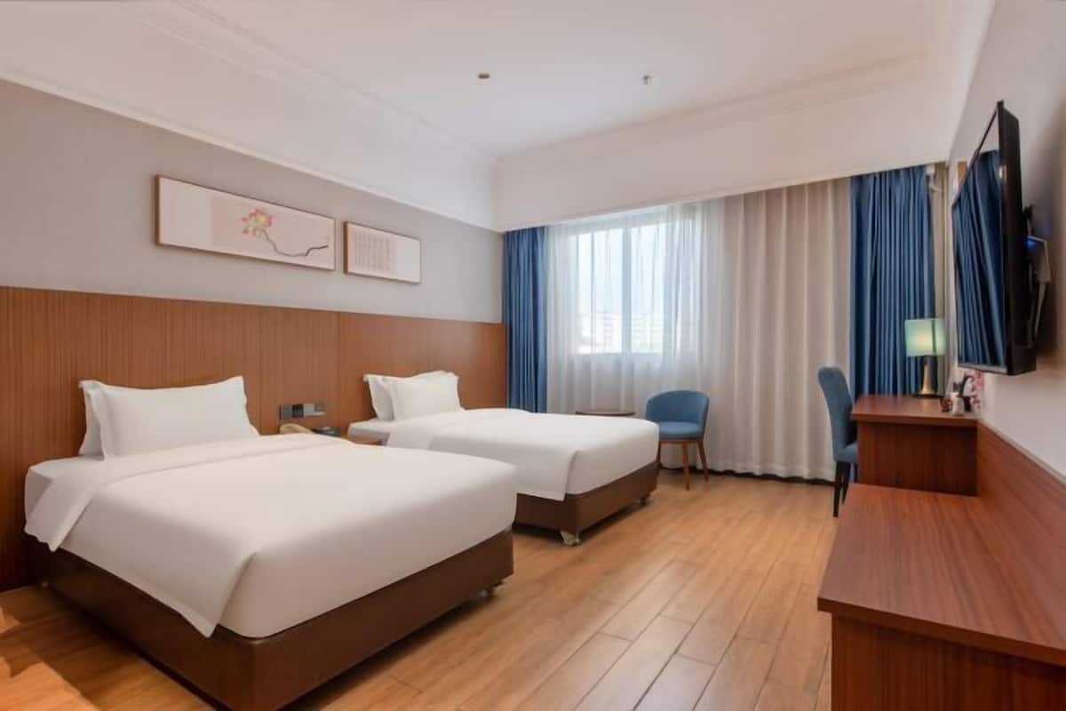A hotel room with two beds, a desk, a chair, a TV, and a window with curtains.