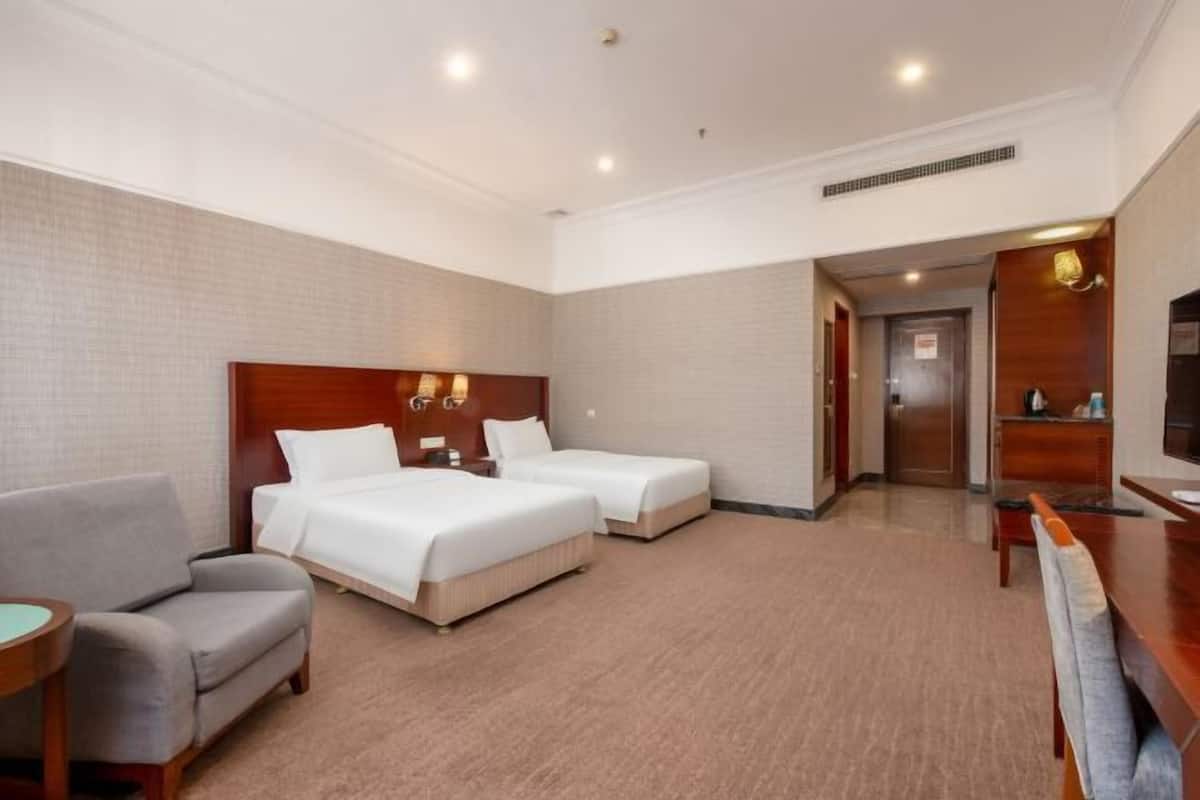 A hotel room with two beds, a sofa, a desk, and a bathroom visible through an open door.