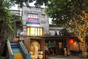A building with a staircase leading to a second-floor balcony, a large elephant sculpture, and a tree with lights. - Carrianna Hotel (Foshan)