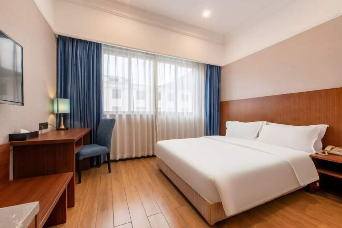 A hotel room with a bed, a desk, a chair, a lamp, and a window with curtains.