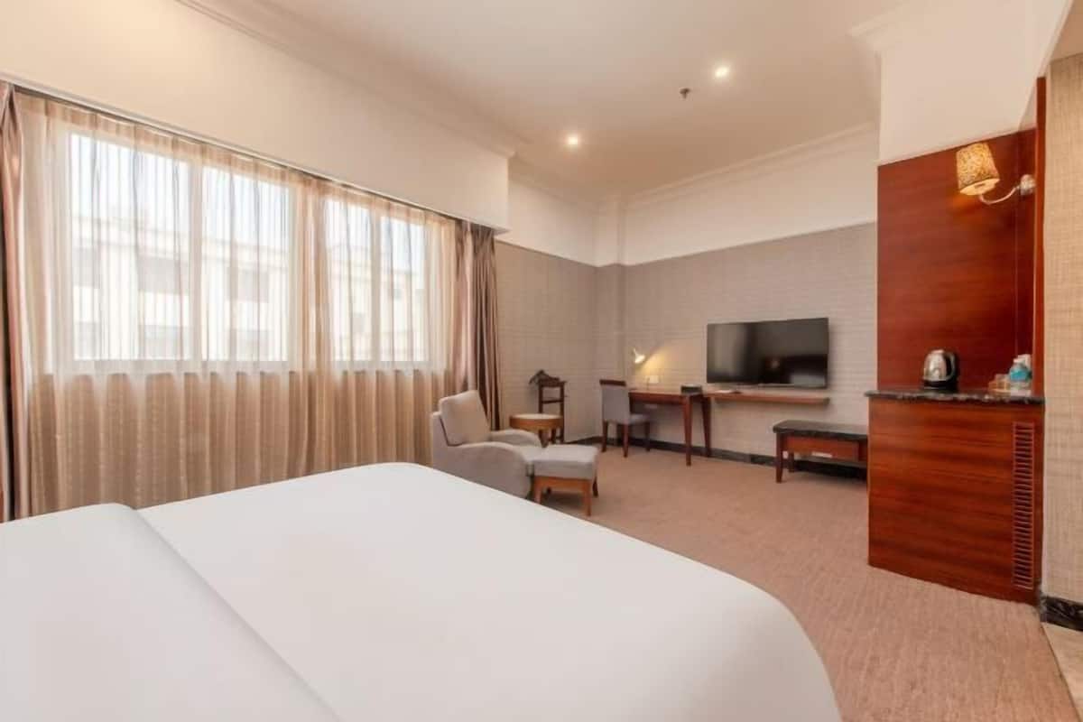 A hotel room with a large bed, a desk with a chair, a television, and a wooden cabinet with a mirror.