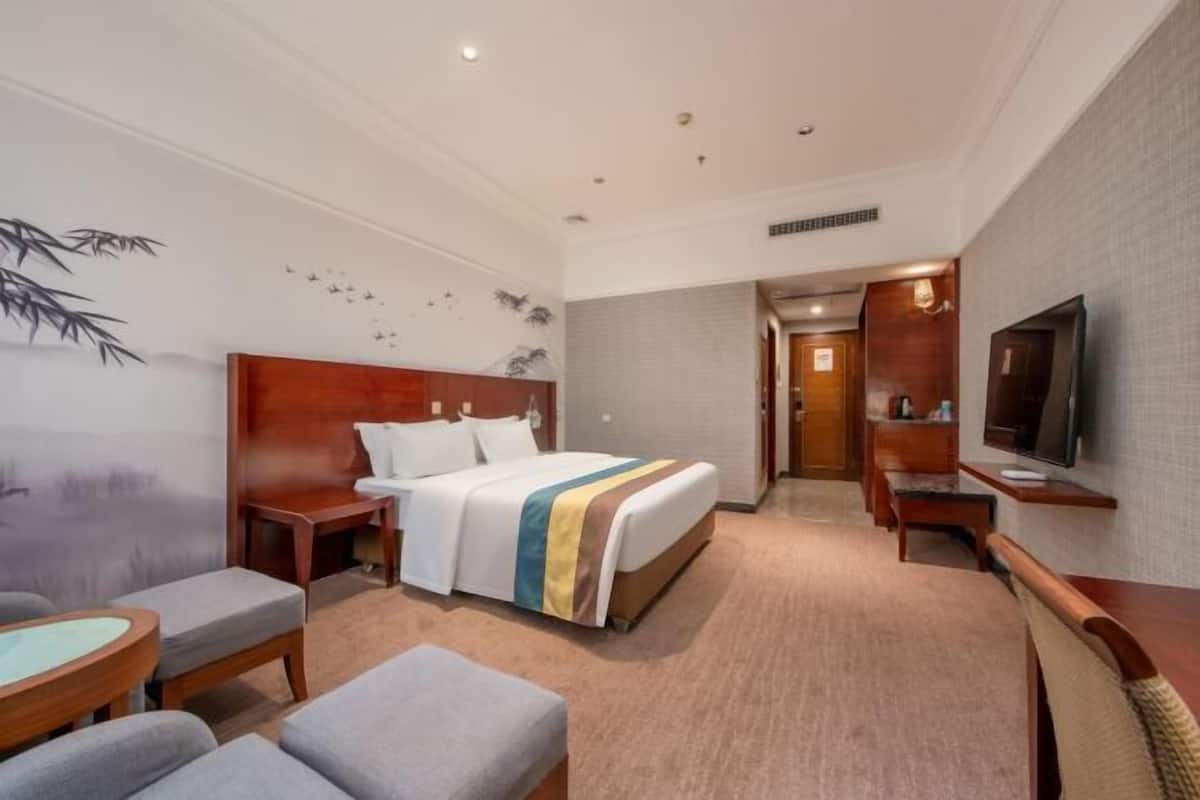 A hotel room with a bed, a desk, a chair, a TV, and a small table.