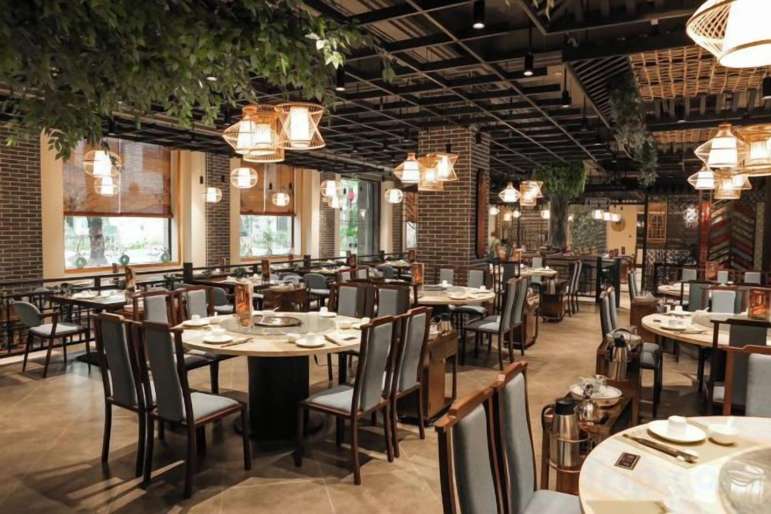 Ein Restaurant mit mehreren Tischen und Stühlen, hängenden Pflanzen und Pendelleuchten.