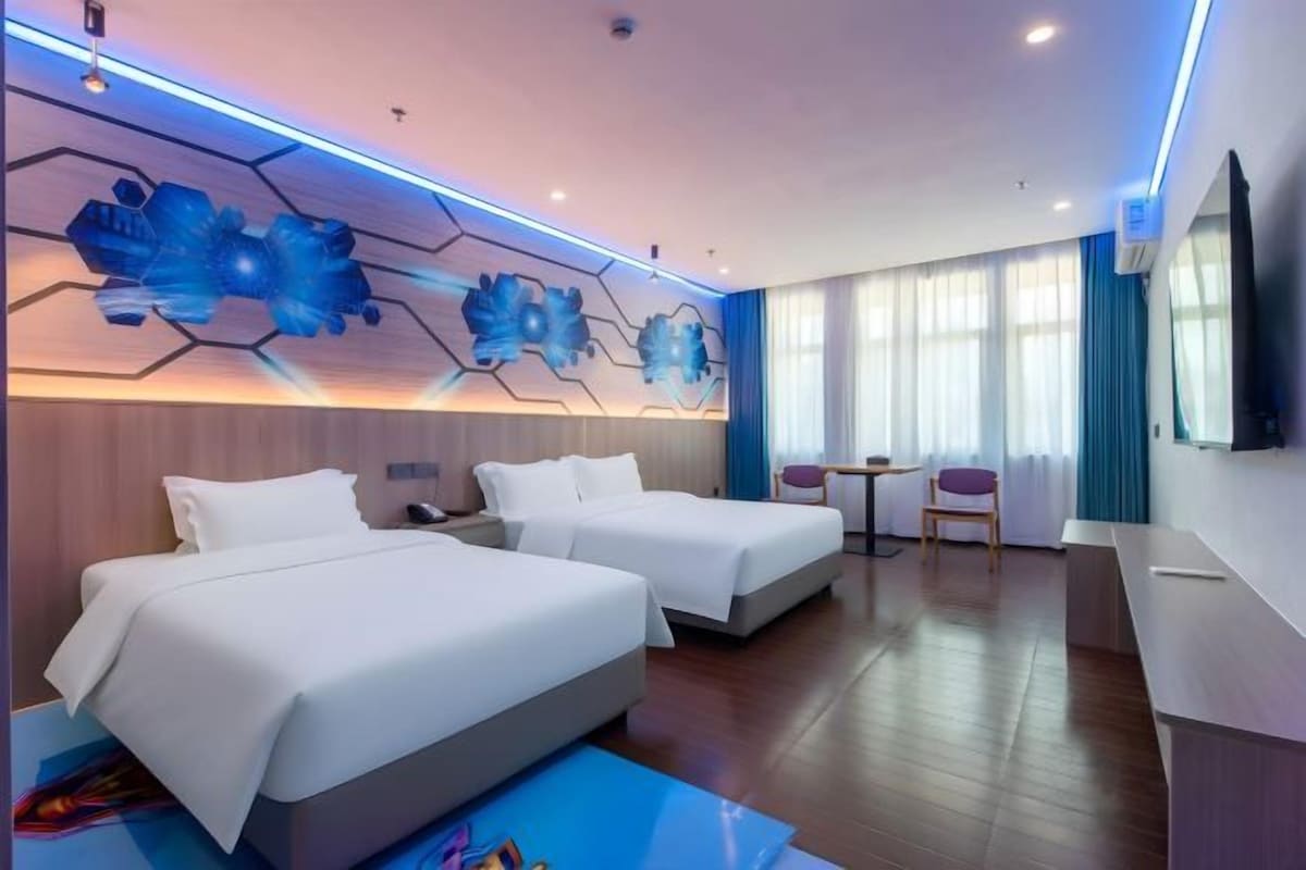 A hotel room with two beds, a desk, a chair, and a large window.