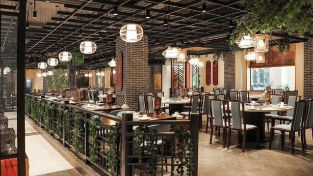 A restaurant with a long counter, multiple tables, and hanging lights. - Carrianna Hotel (Foshan)