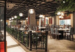 A restaurant with a long counter, multiple tables, and hanging lights.