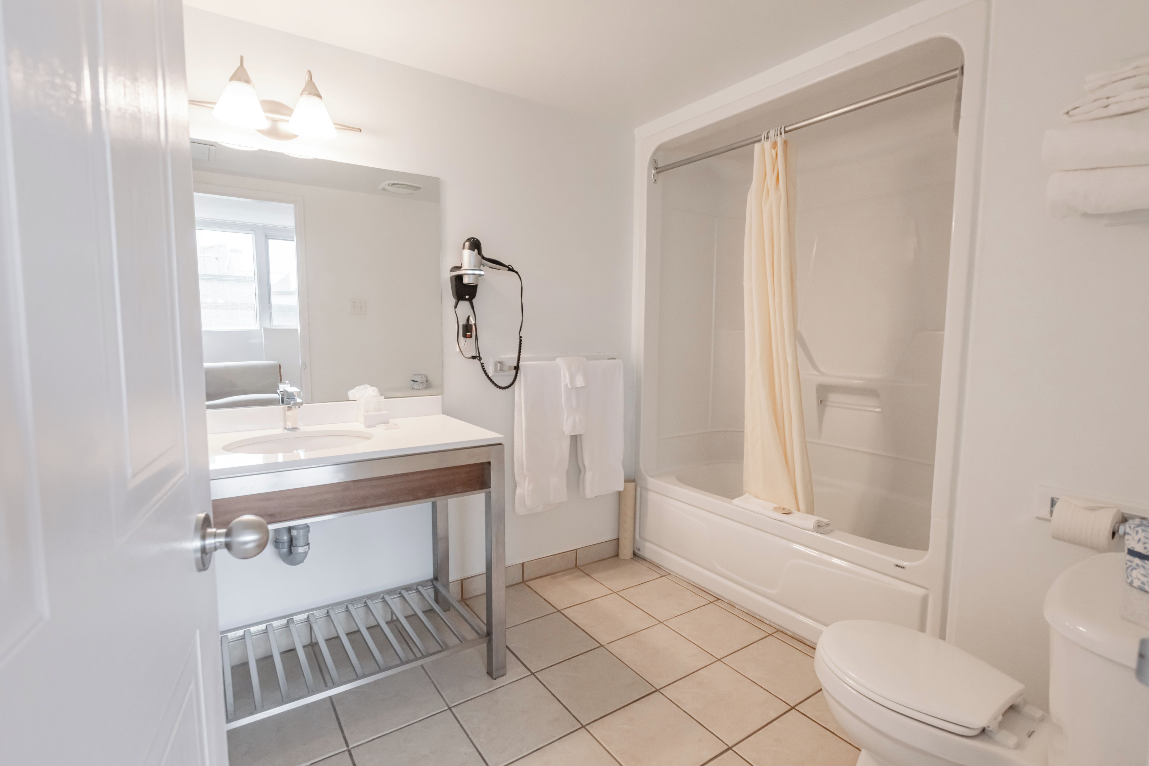 A bathroom with a shower, toilet, sink, and a hairdryer mounted on the wall.