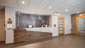 A reception desk with a wooden counter, a grey wall, and a sign indicating the room number.