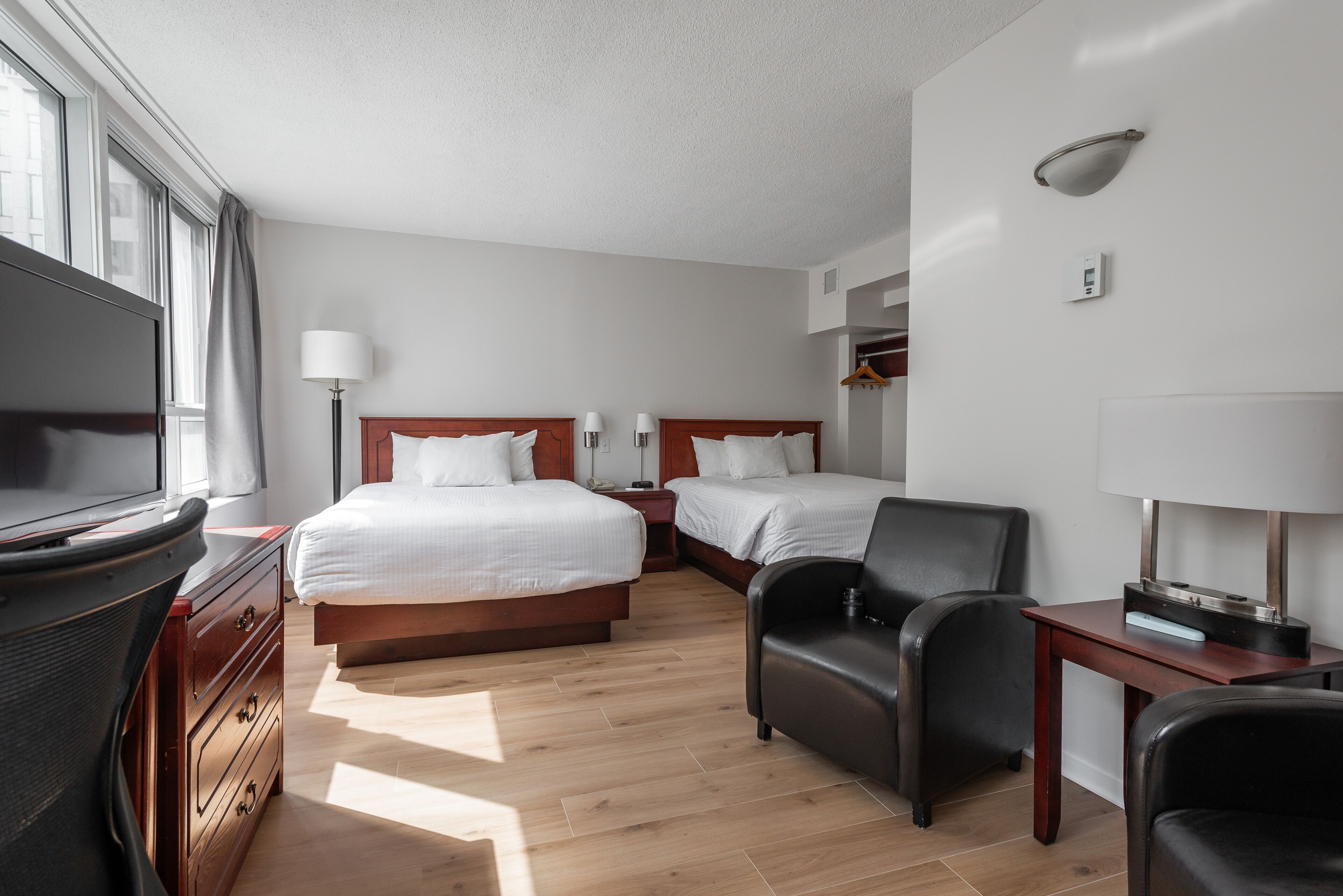 A hotel room with two beds, a TV, a desk, a chair, and a lamp.
