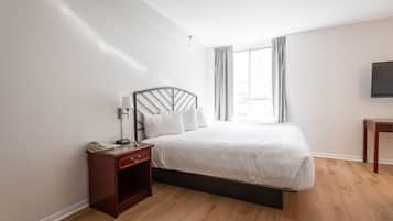 A bedroom with a bed, bedside table, lamp, and a television on the wall.