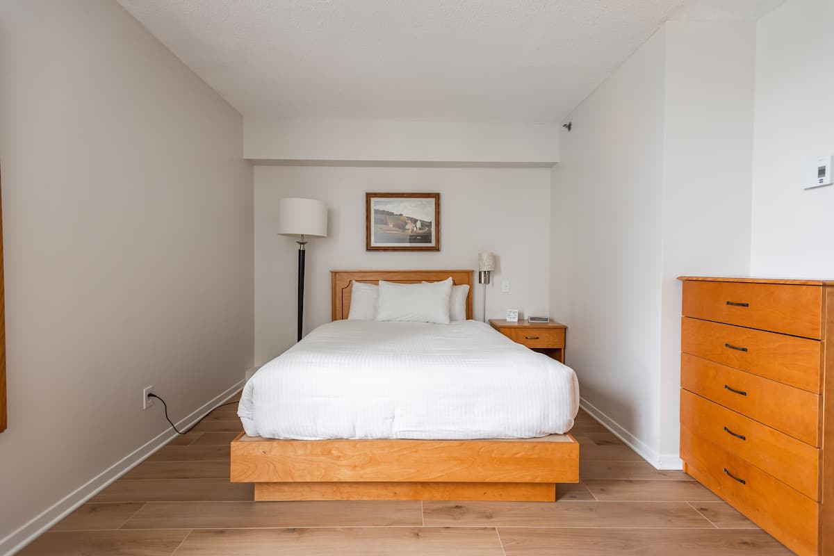 A bedroom with a wooden bed, a nightstand, a dresser, and a wall-mounted lamp.
