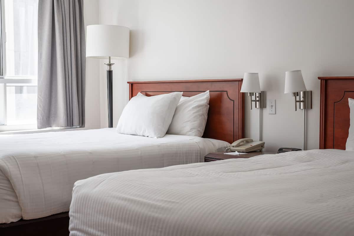 A hotel room with two beds, a nightstand with a phone, and wall-mounted lamps.