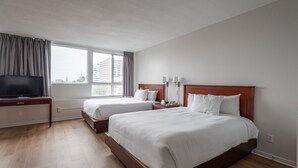 A hotel room with two beds, a TV, a desk, and a window with curtains.