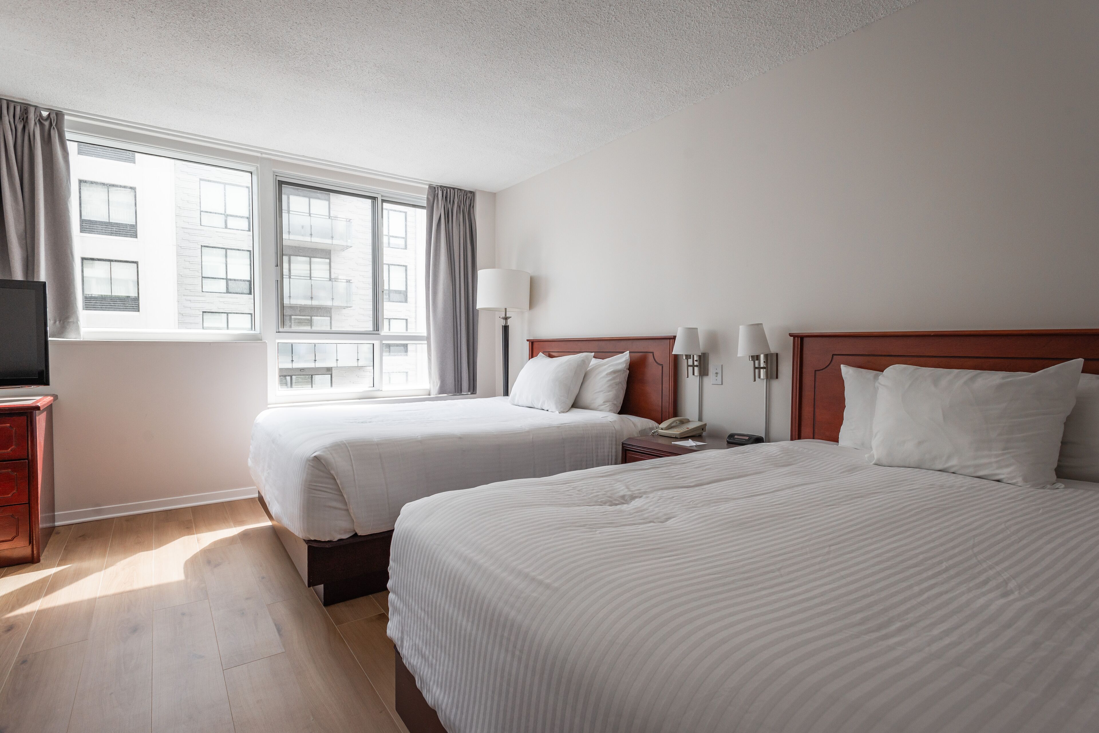 A hotel room with two beds, a TV, a bedside table, and a window with curtains.