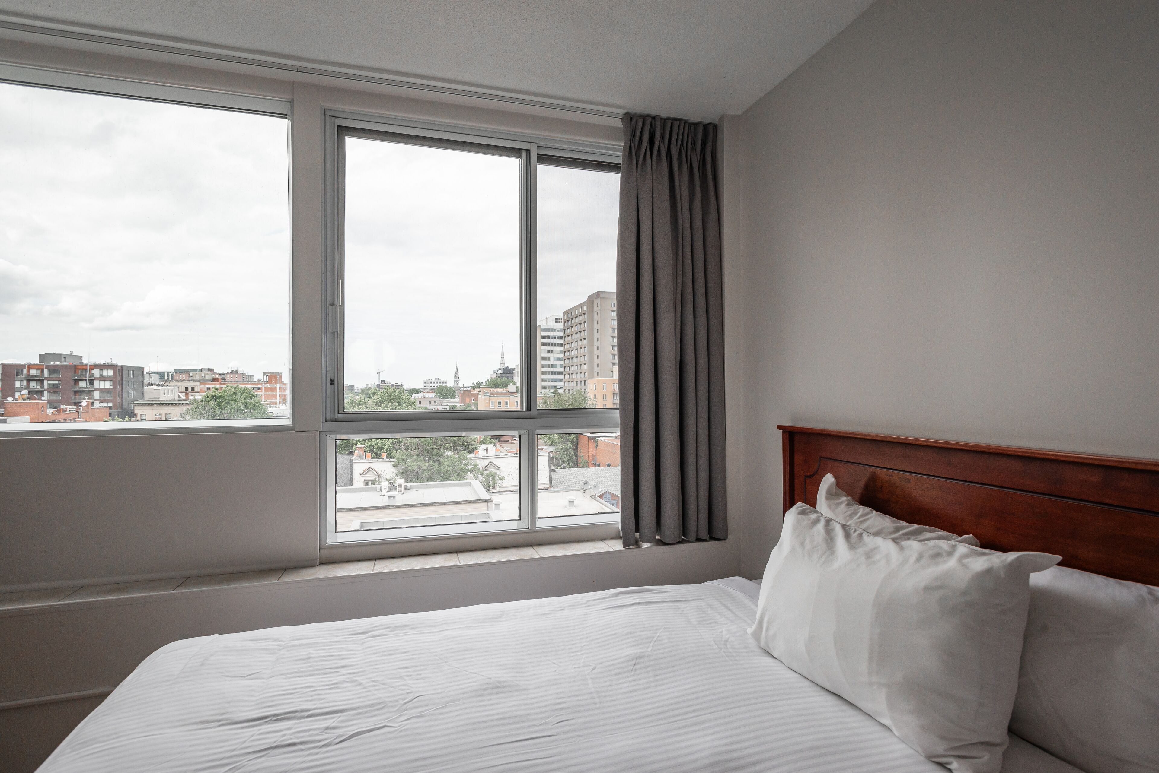 Une chambre d’hôtel avec une grande fenêtre, une tête de lit en bois et un lit parfaitement fait.