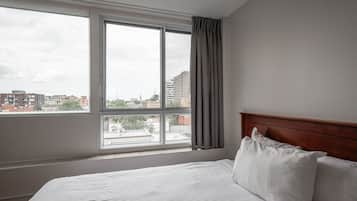 Une chambre d’hôtel avec une grande fenêtre, une tête de lit en bois et un lit parfaitement fait.