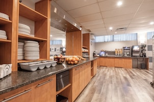 A modern kitchen with wooden cabinets, a marble countertop, and various food items displayed.