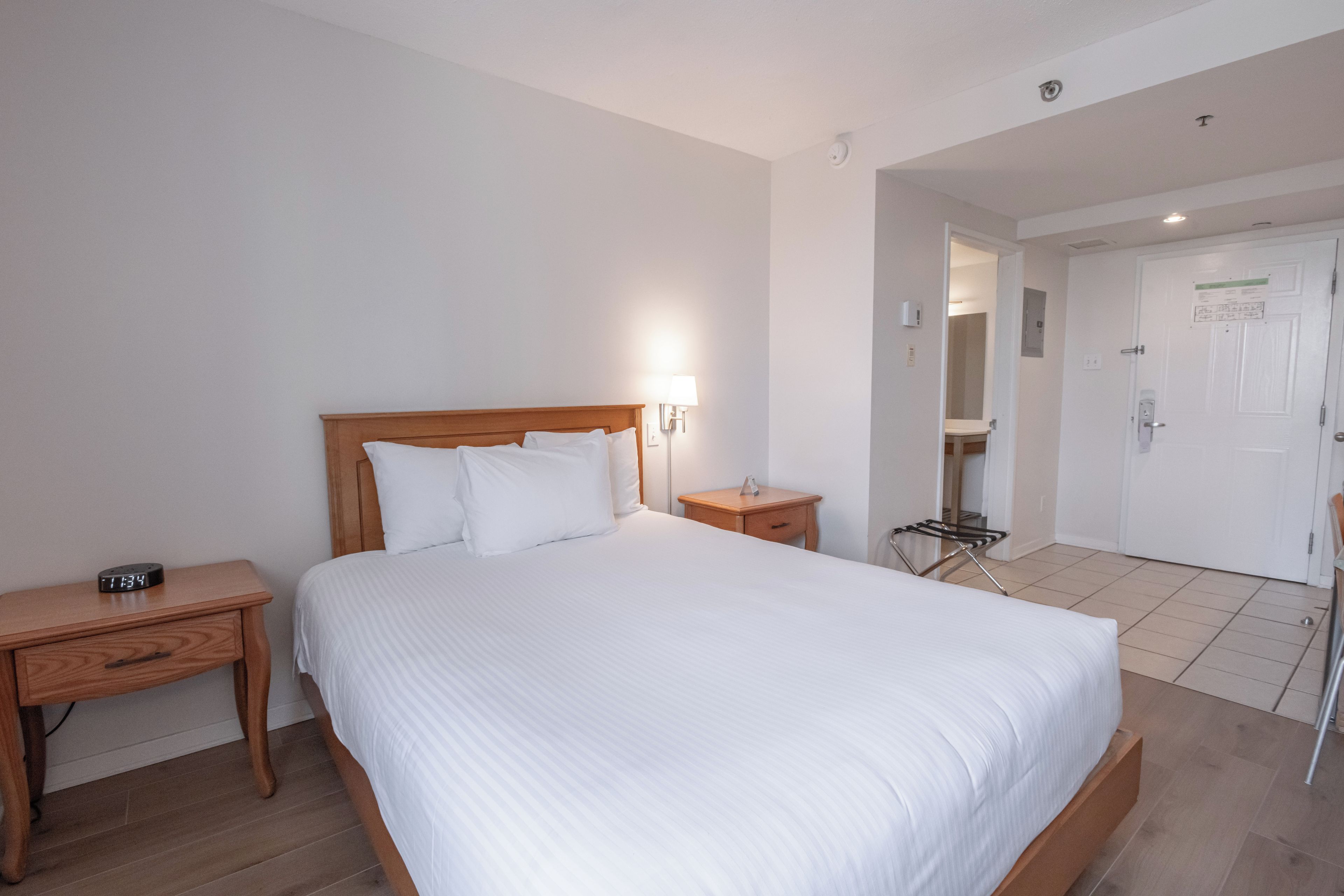 A hotel room with a large bed, a bedside table, a nightstand, a lamp, and a door leading to a bathroom.