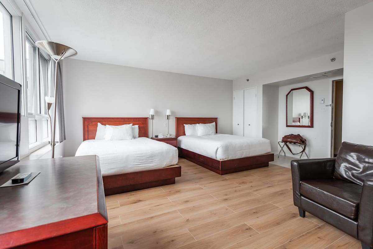 A hotel room with two beds, a desk, a TV, and a leather sofa.