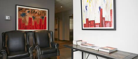 Un hall con dos sillones de cuero negro, una mesa con revistas y dos grandes cuadros abstractos en las paredes.