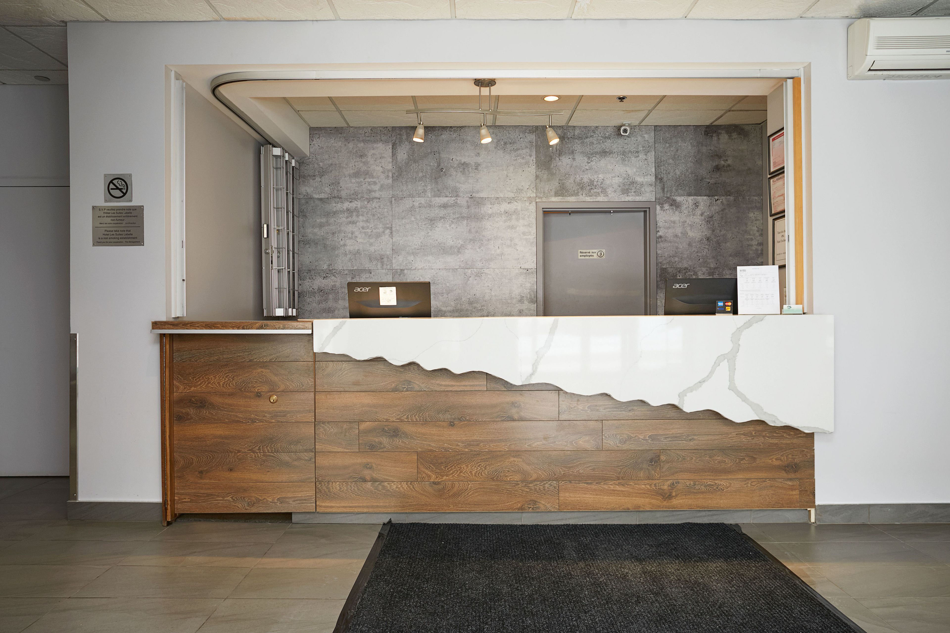 Una reception con una finitura in legno e un piano d'appoggio effetto marmo bianco. Sullo sfondo, una parete grigia con una porta.
