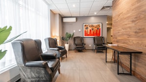 A modern waiting area with leather chairs, a wooden reception desk, and a large abstract painting on the wall.