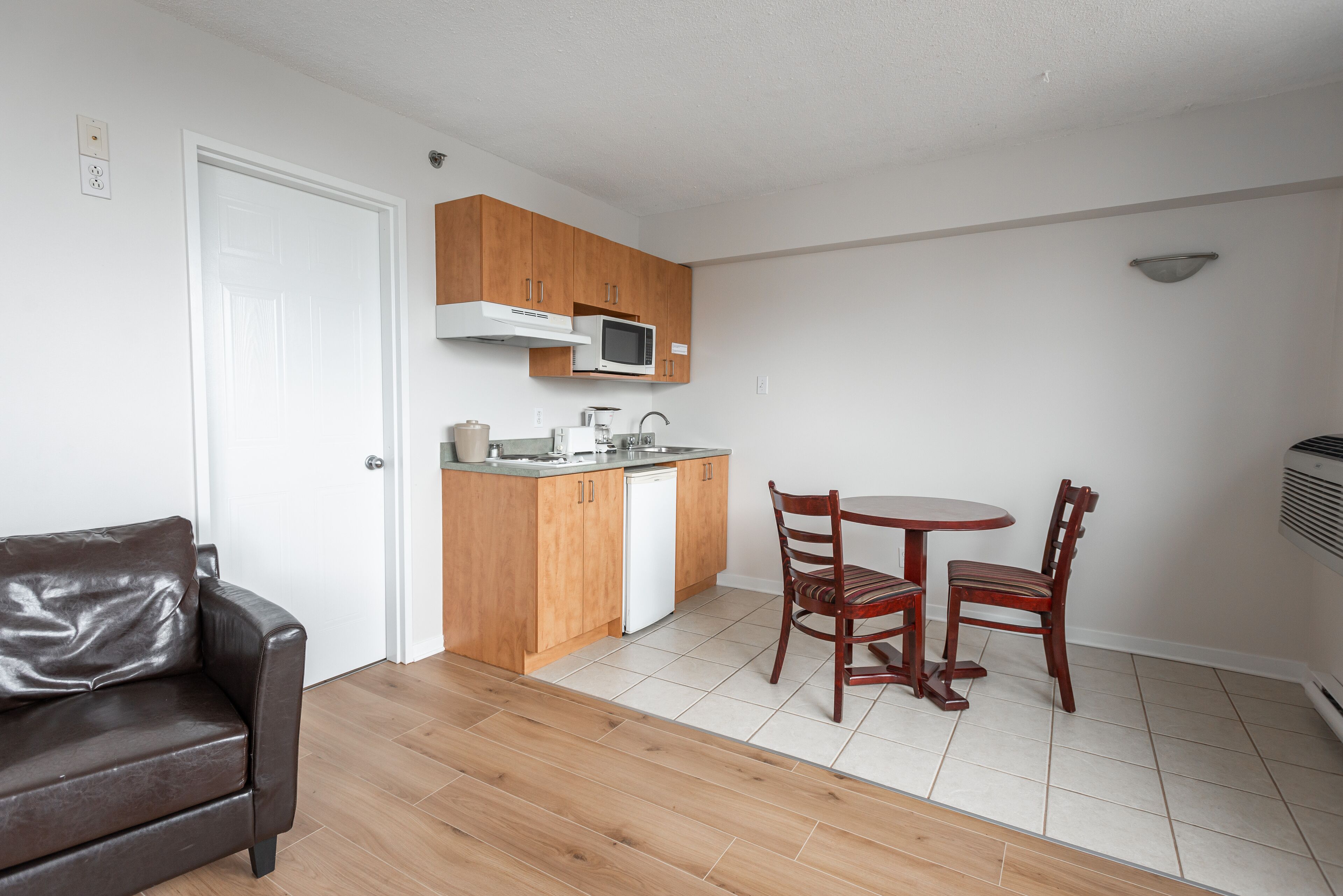 Un espacio habitable compacto con kitchenette, una zona de comedor con dos sillas y un sofá de cuero marrón.