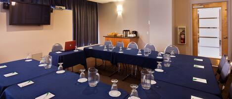 A conference room with a long table set for a meeting, equipped with nameplates, water glasses, and a coffee station.