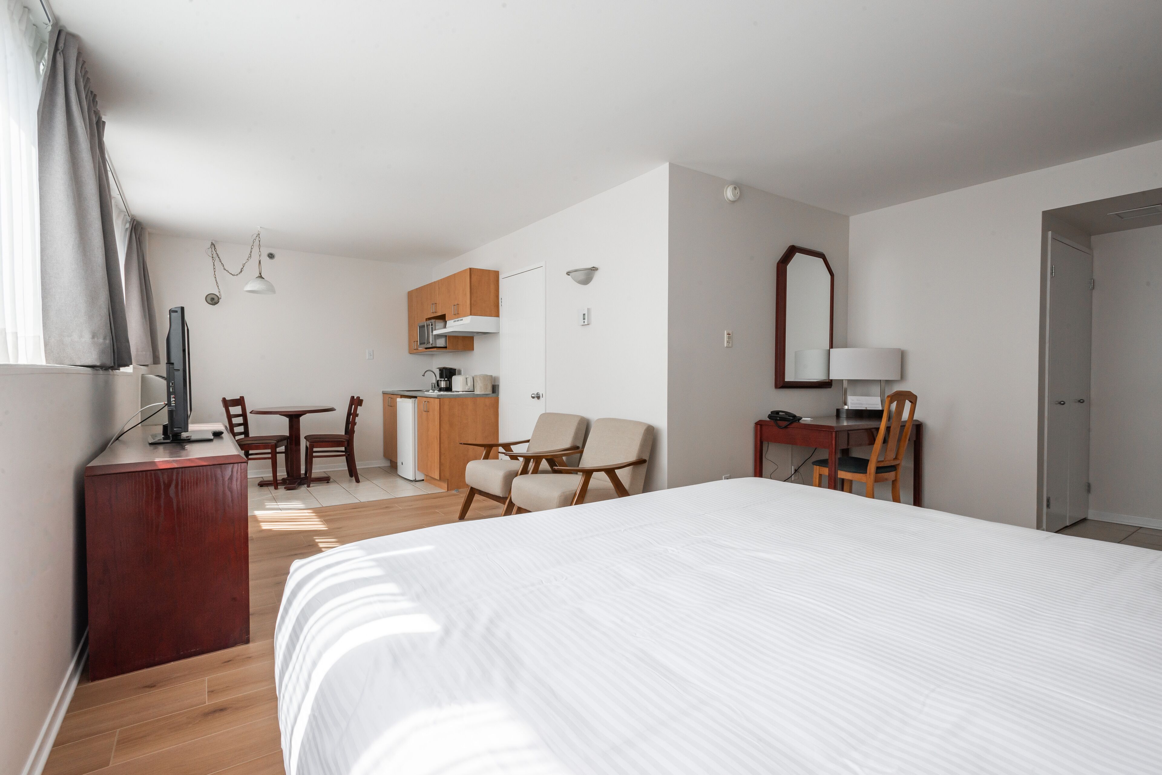 A hotel room with a large bed, a desk with a chair, a kitchenette, and a bathroom.