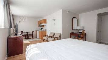 A hotel room with a large bed, a desk with a chair, a kitchenette, and a bathroom.
