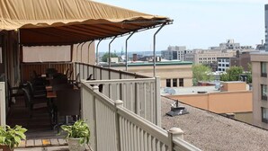 A rooftop terrace with a covered seating area, a railing, and a view of the cityscape.