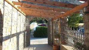 A stone pathway leading to a wooden pergola with a view of a mountainous landscape. - Creta Suites (Ierapetra)