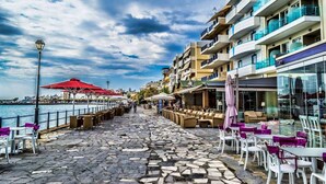 A coastal promenade with outdoor seating, a view of the sea, and multi-story buildings with balconies. - Creta Suites (Ierapetra)