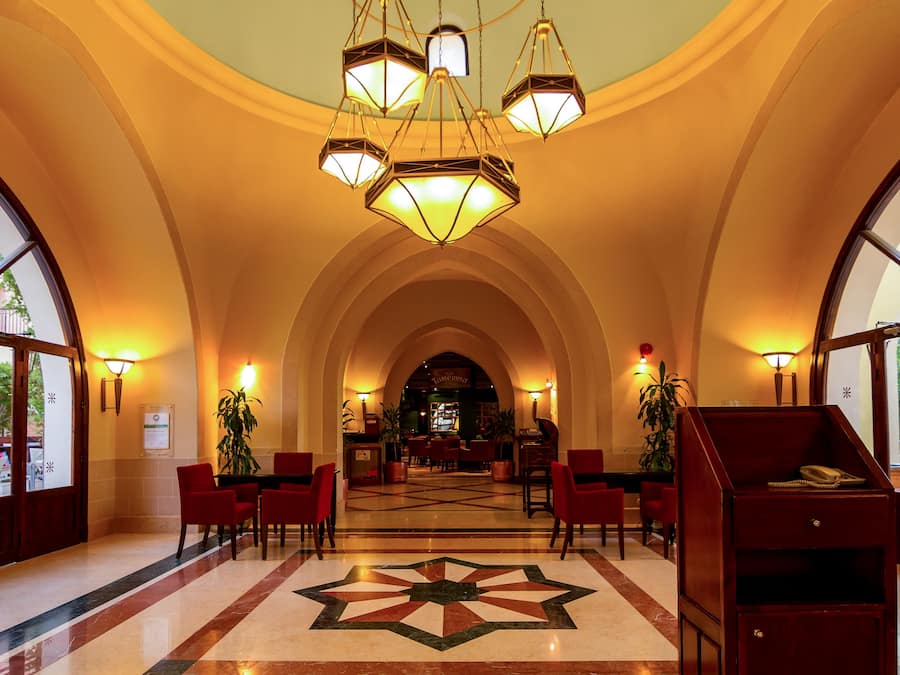 Vestíbulo de hotel con suelo estampado con motivos de estrellas, sillas rojas, un mostrador de recepción y una escalera.