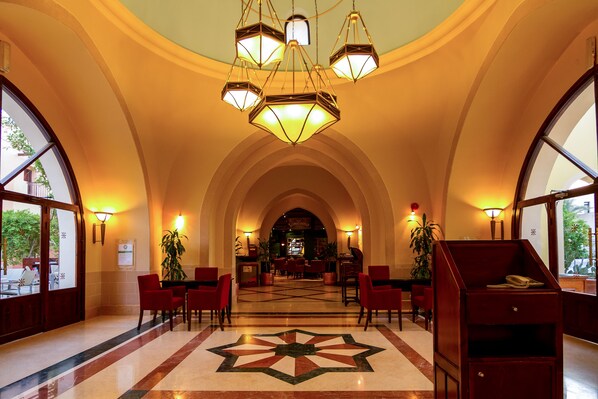 A hotel lobby with a star-patterned floor, red chairs, a reception desk, and a staircase. - JAZ Makadi Saraya Resort - All inclusive (Makadi Bay)