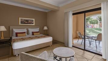 Habitación de hotel con cama, dos lámparas de noche, una mesa redonda y vistas a un patio exterior con sillas.