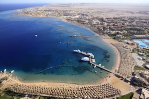 Vista aérea de un complejo turístico costero con un puerto deportivo, playa y edificios del complejo.
