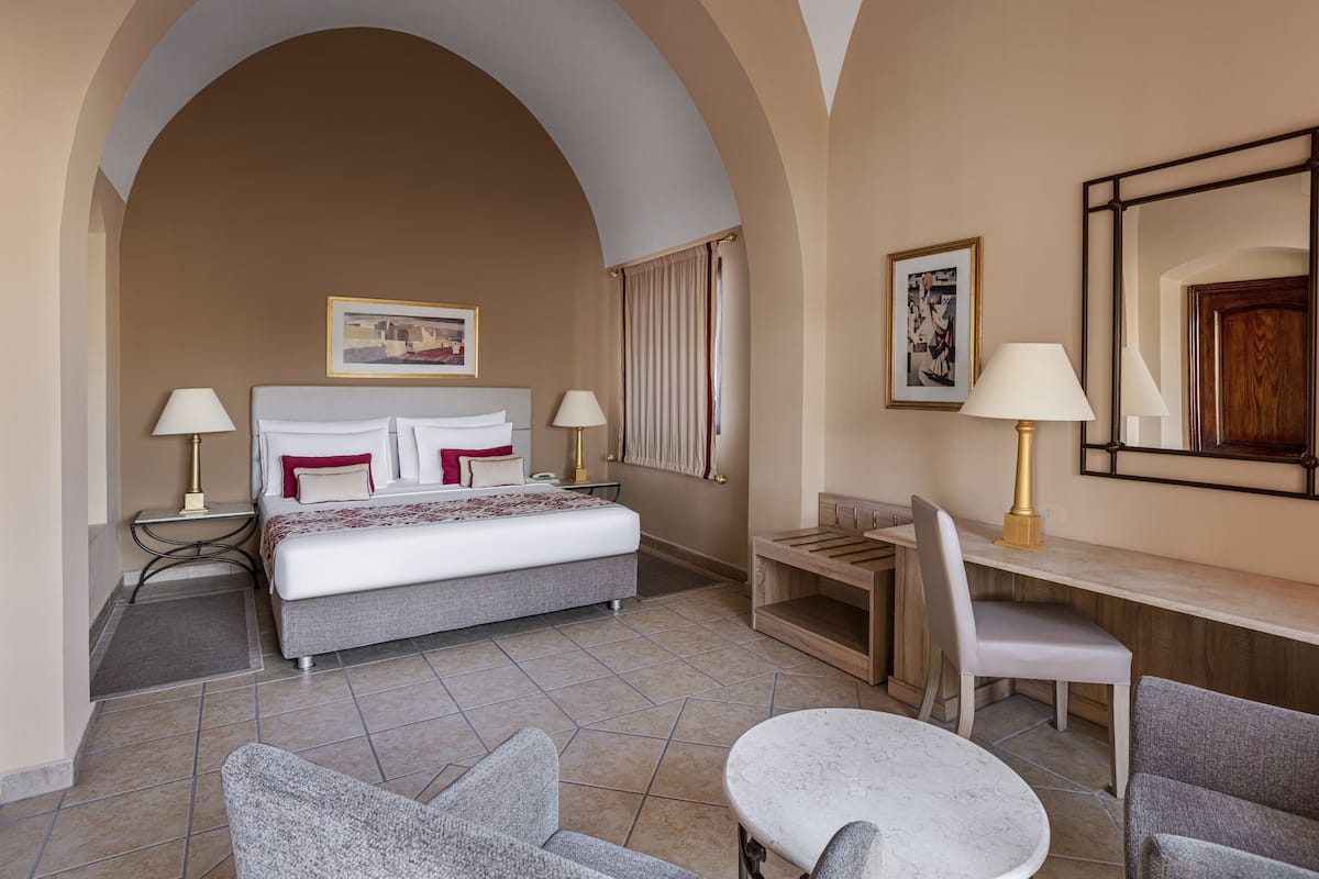Habitación de hotel con cama, dos mesitas de noche con lámparas, un escritorio con silla y un espejo grande.