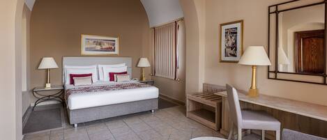 A hotel room with a bed, two bedside tables with lamps, a desk with a chair, and a large mirror.