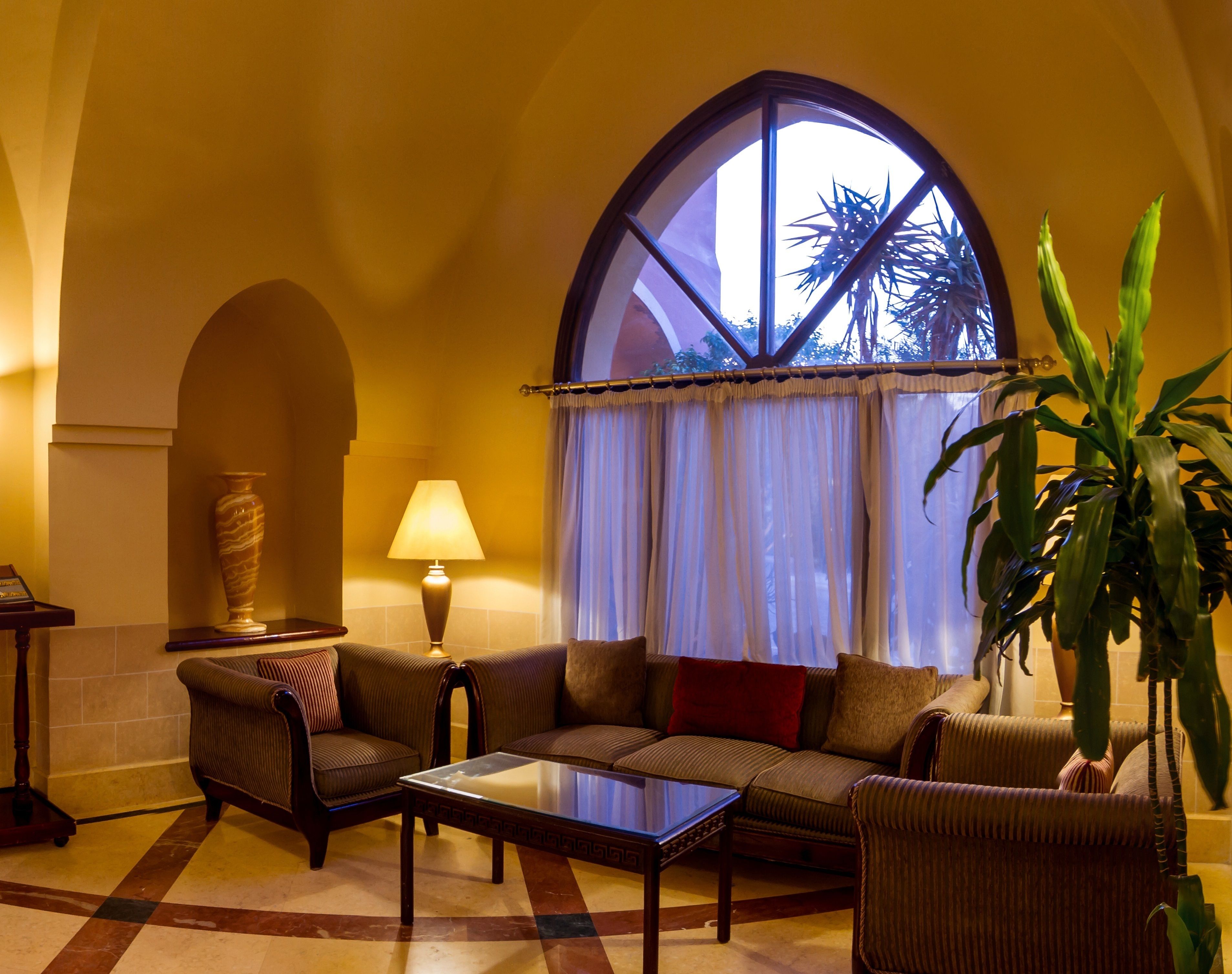 A cozy living room with a sofa set, a coffee table, a lamp, and a large window with curtains.