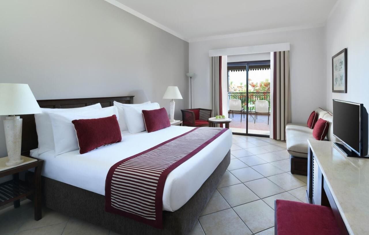 Quarto de hotel com cama, televisão, escrivaninha e varanda com vista.