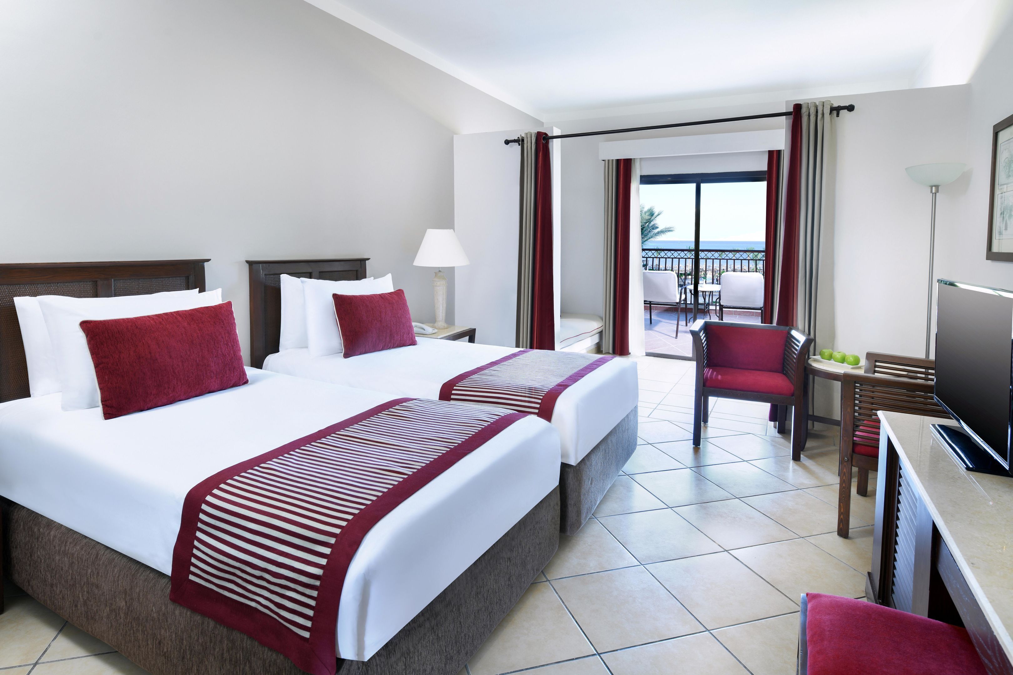 Une chambre d’hôtel avec deux lits, un balcon, une télévision et un coin repas.