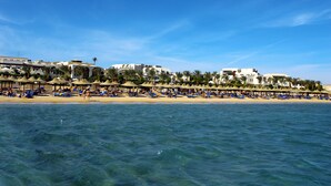 Un resort en la playa con hileras de tumbonas y sombrillas, una playa de arena y edificios con balcones que dan al mar.