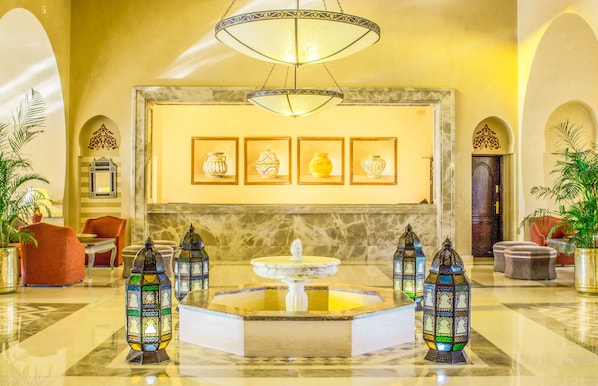 Un hall d’entrée agrémenté d’une fontaine en marbre, de lanternes décoratives, d’œuvres d’art encadrées et de sièges confortables.